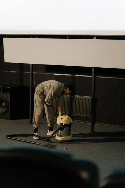 Close-up of a person vacuuming a patterned pillow on a dark sofa indoors.